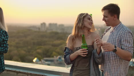 Young-couple-is-dancing-on-the-roof-with-beer-on-the-party.-They-enjoy-the-moment-with-each-other-on-the-roof-at-sunset.